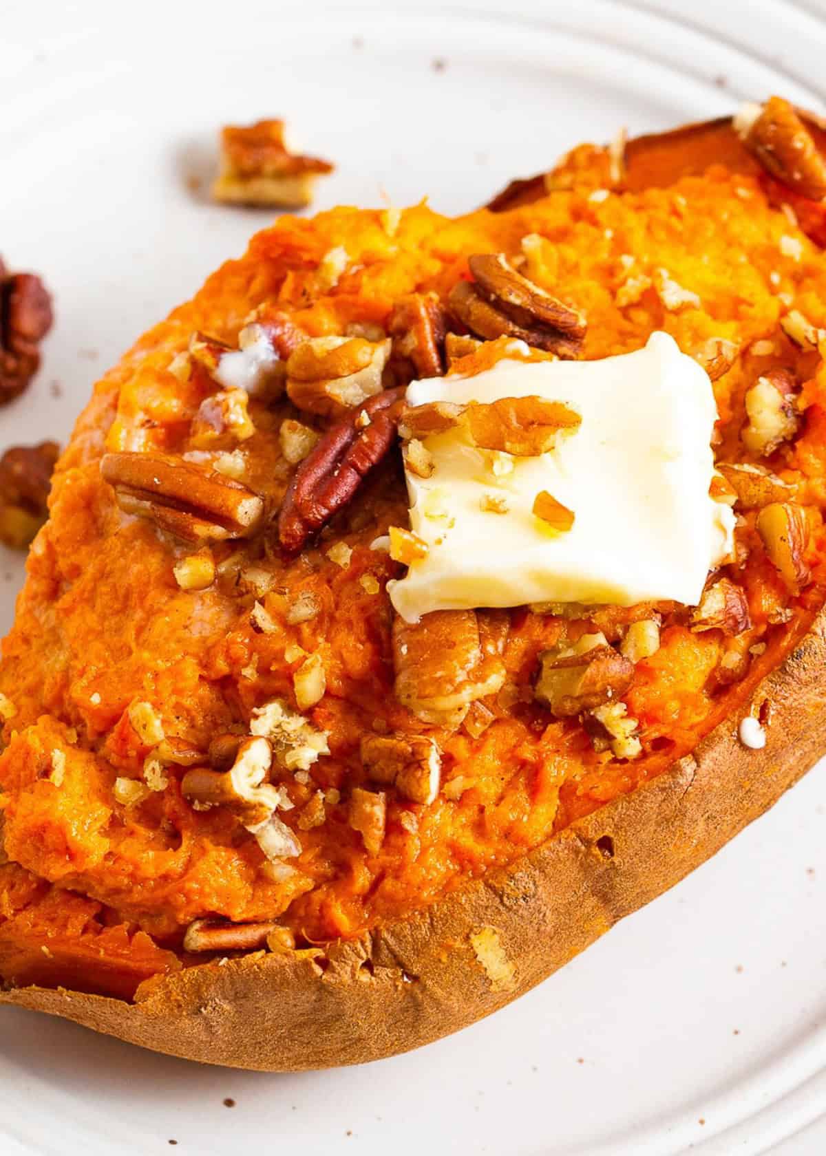 A baked sweet potato topped with pecans and a pat of melting butter on a white plate.