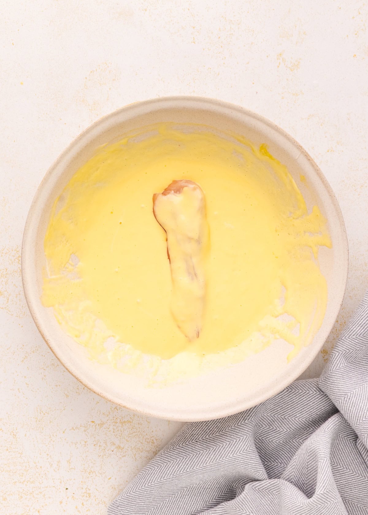 Air Fryer Chicken Tenders dipped in yellow batter, served in a bowl with a gray cloth beside.