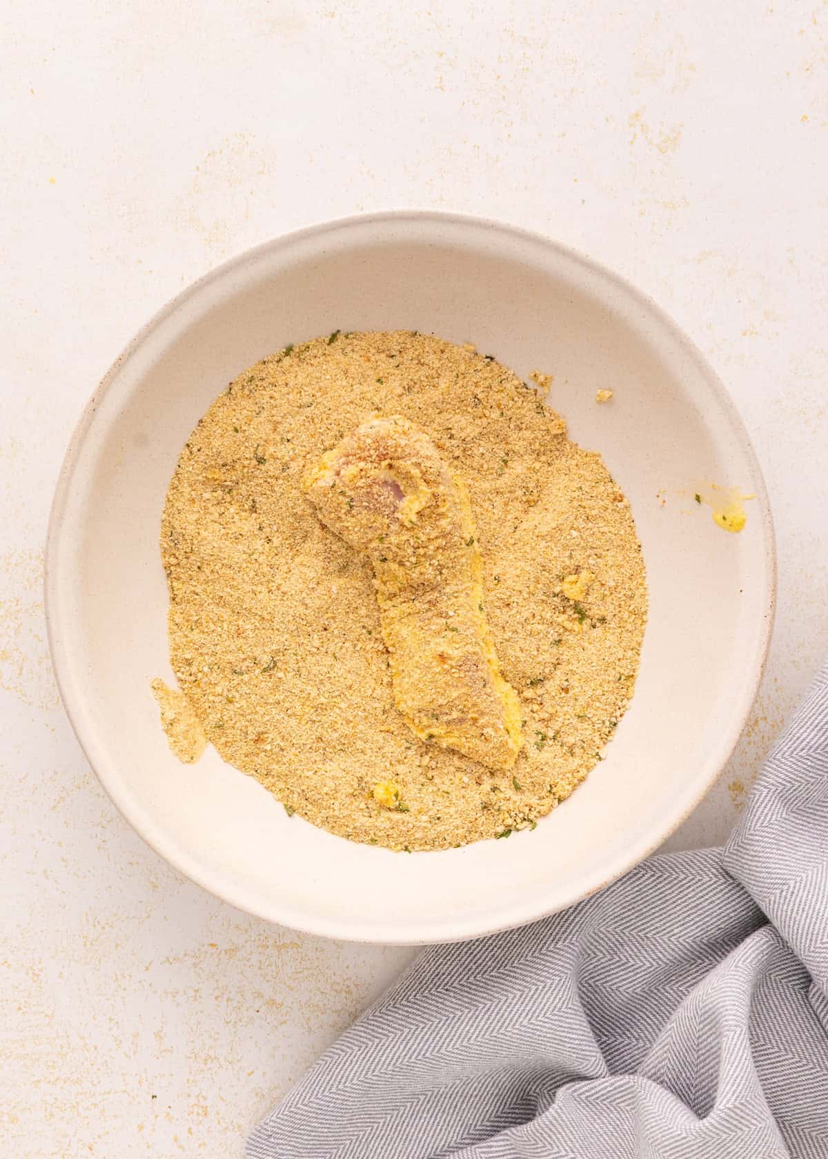 A crispy Air Fryer Chicken Tenders drumstick sits in a shallow white bowl on a light surface.