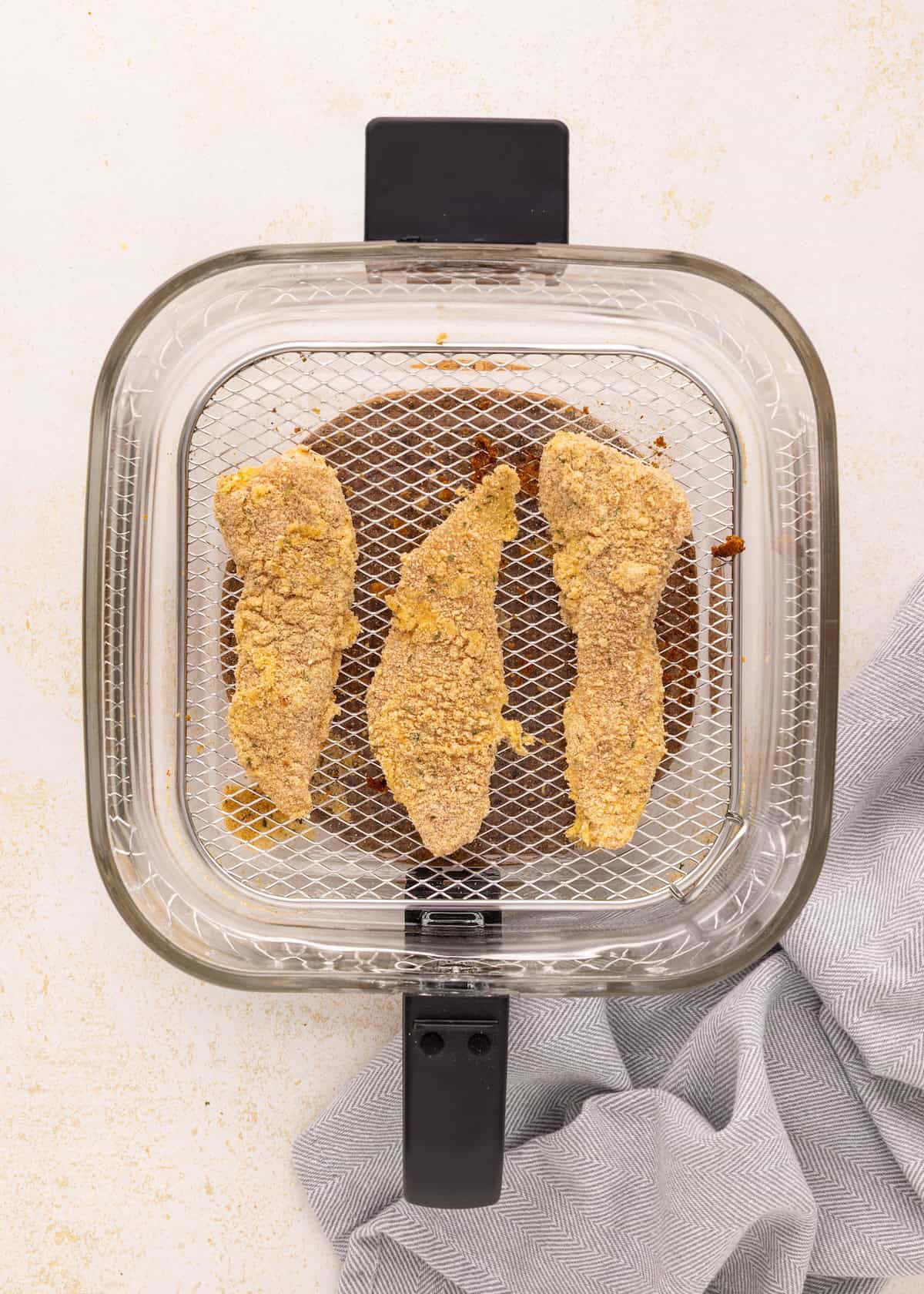Air Fryer Chicken Tenders: Three breaded tenders in an air fryer basket, viewed from above.