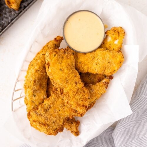 Air Fryer Chicken Tenders: crispy breaded tenders on parchment with a cup of dipping sauce.
