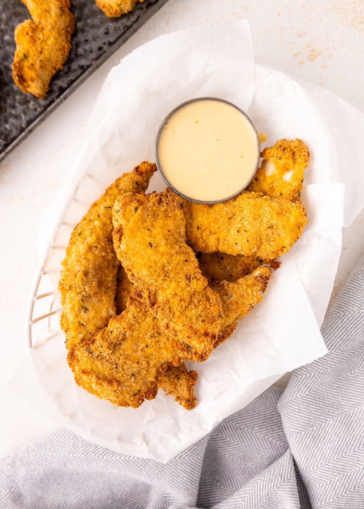 Air Fryer Chicken Tenders: crispy breaded tenders on parchment with a cup of dipping sauce.