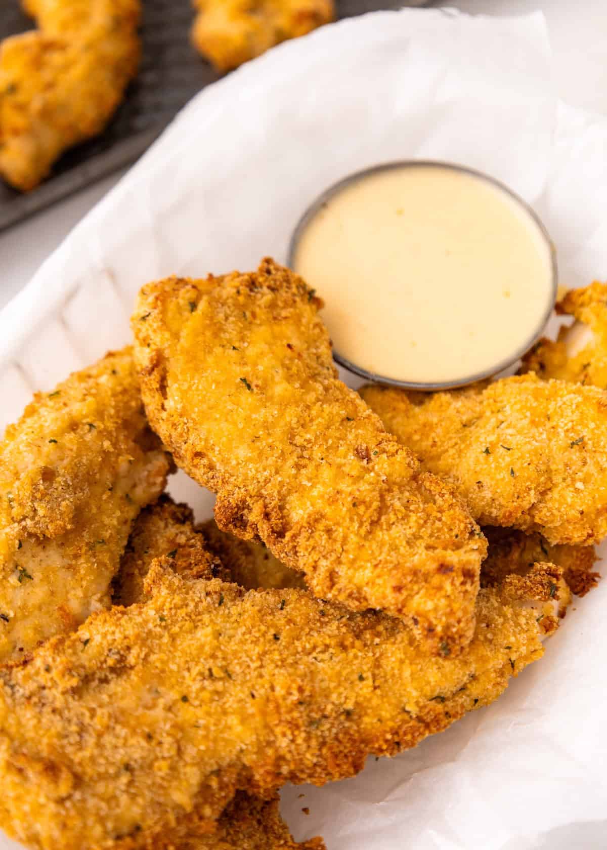 Air Fryer Chicken Tenders on parchment paper with a small cup of dipping sauce.