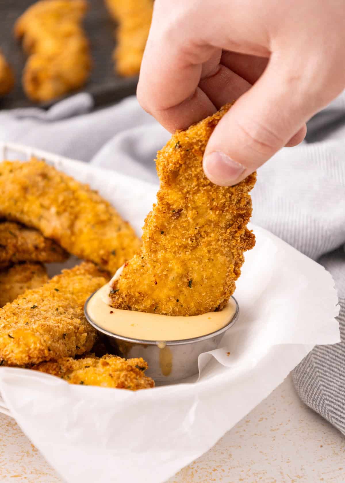 A hand dips an Air Fryer Chicken Tender into a cup of creamy dipping sauce.