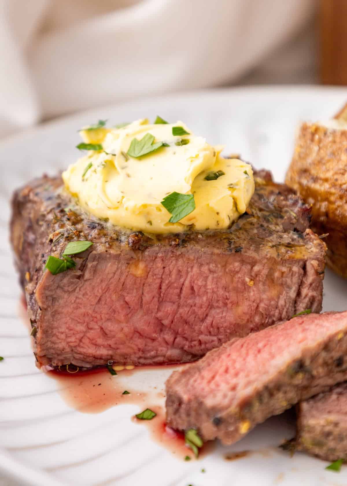Juicy steak topped with herb butter, garnished with parsley, and served with potato.