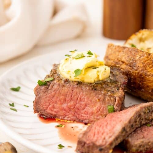 A juicy steak with herb butter and parsley, served with bread on a white plate.