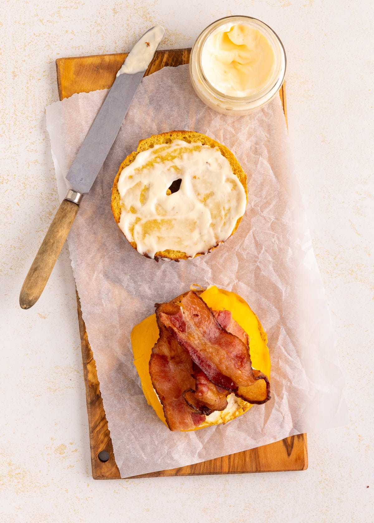 Open sandwich with bacon, cheddar, and mayo on a bun, next to a jar of mayonnaise and knife.