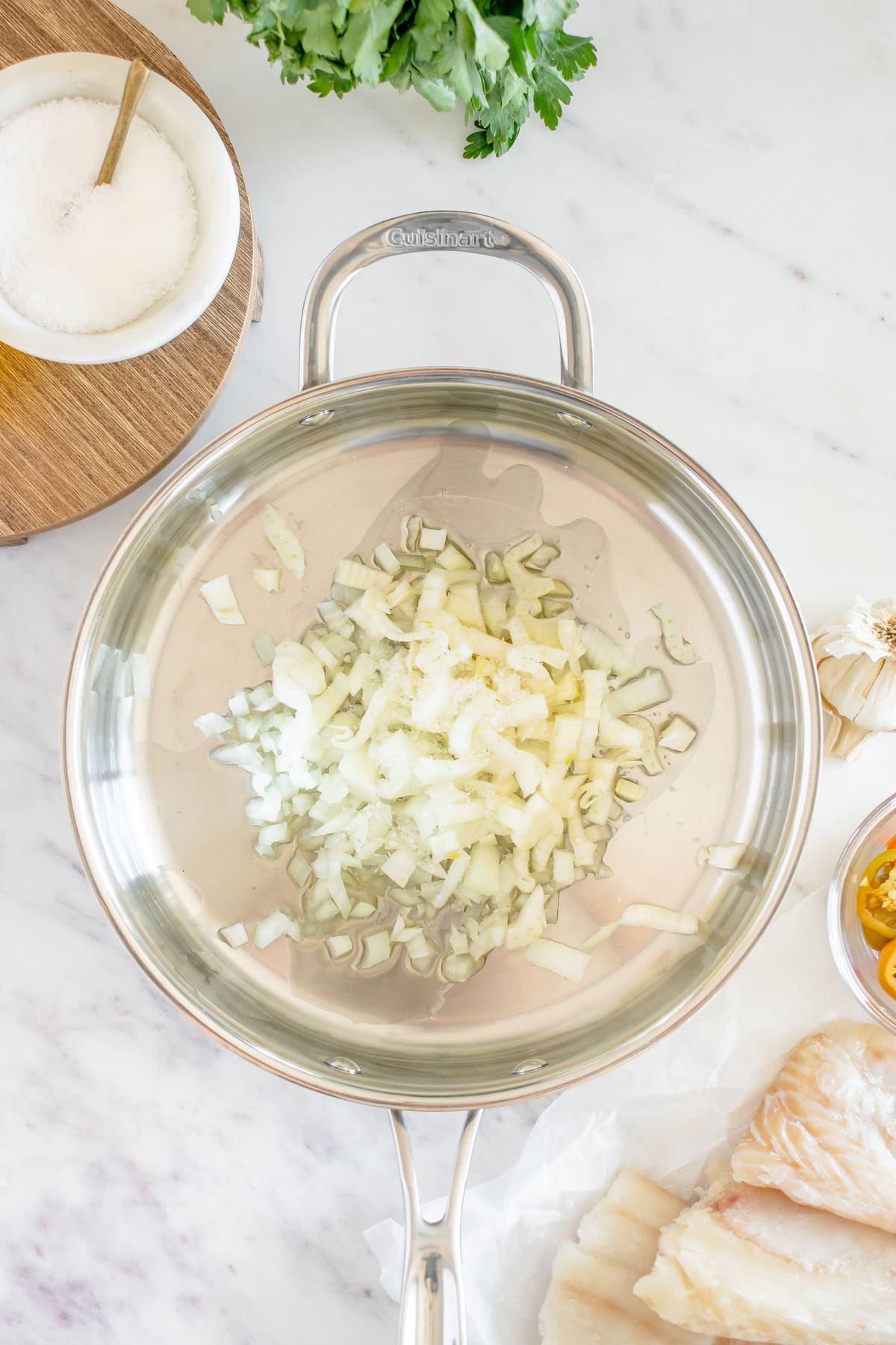 Diced onions in a stainless steel pan, ready to be cooked, with ingredients nearby.