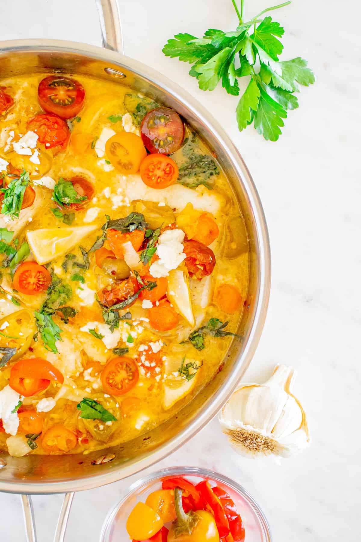 A pan of tomato basil pasta with feta cheese, fresh herbs, and garlic on a marble surface.
