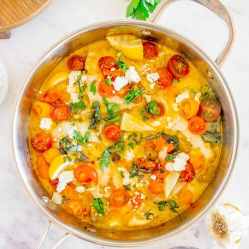 A pan of tomato basil pasta with cheese, surrounded by fresh herbs and ingredients.