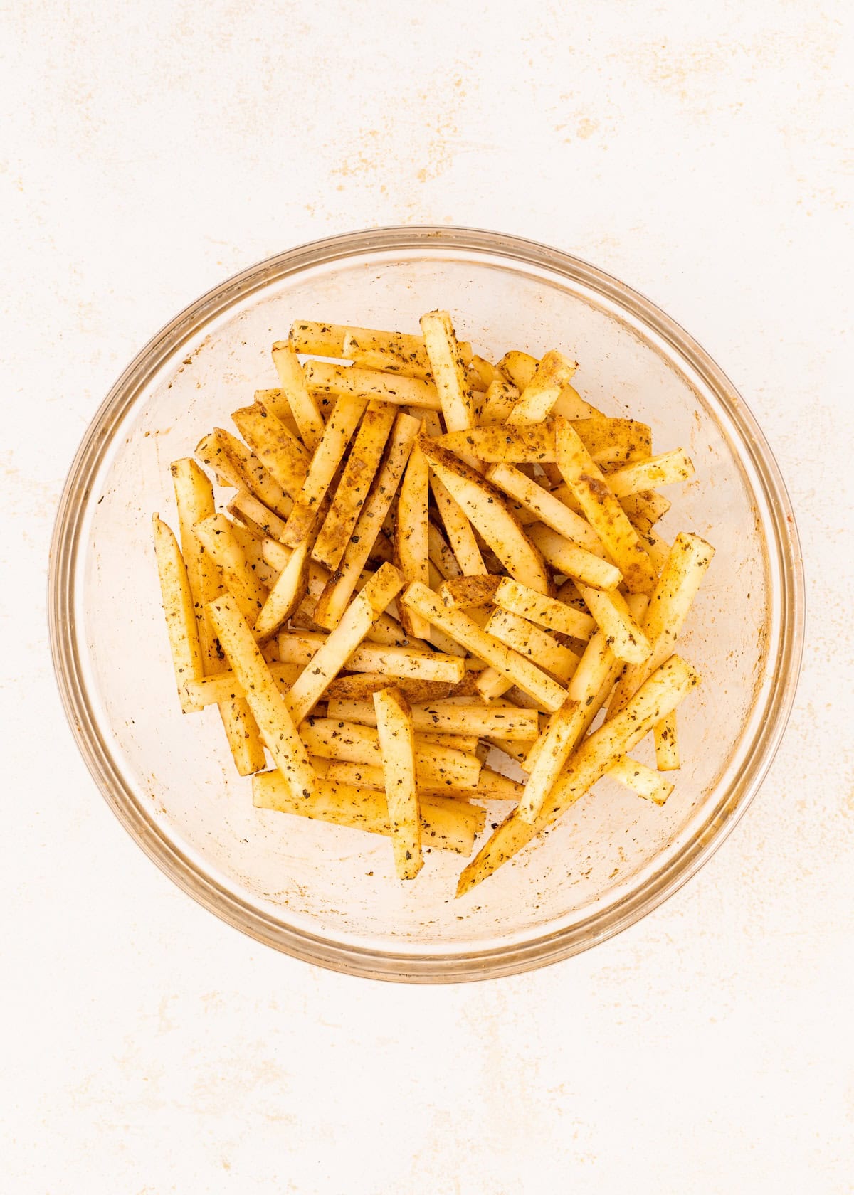 A glass bowl filled with seasoned, uncooked jicama fries on a white background.