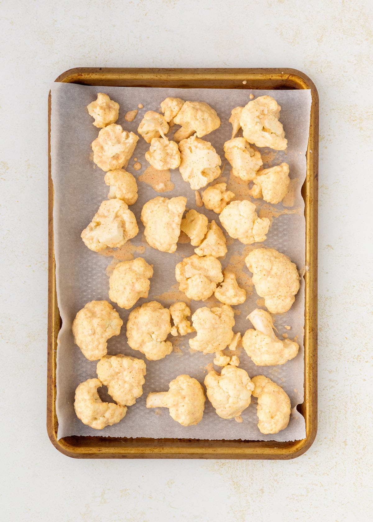 Buffalo Cauliflower Wings coated in batter on a parchment-lined baking sheet.
