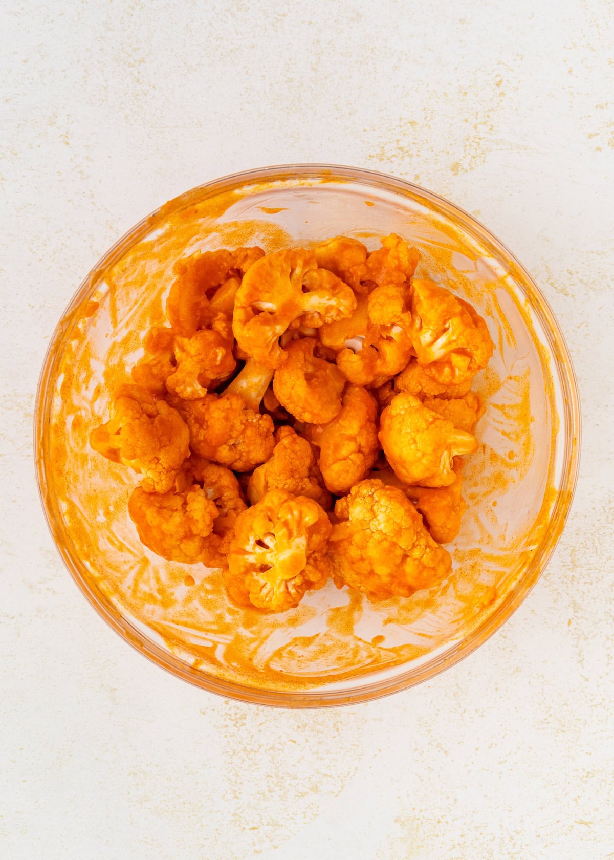 Buffalo Cauliflower Wings coated in orange buffalo sauce in a glass bowl on a light surface.