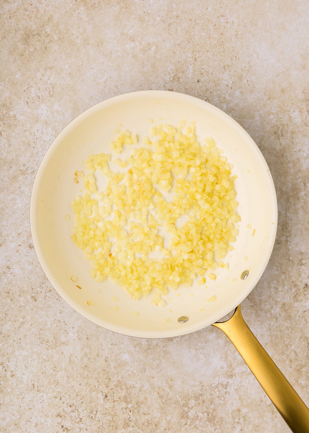 A white skillet with chopped onions being sautéed on a light-colored countertop.