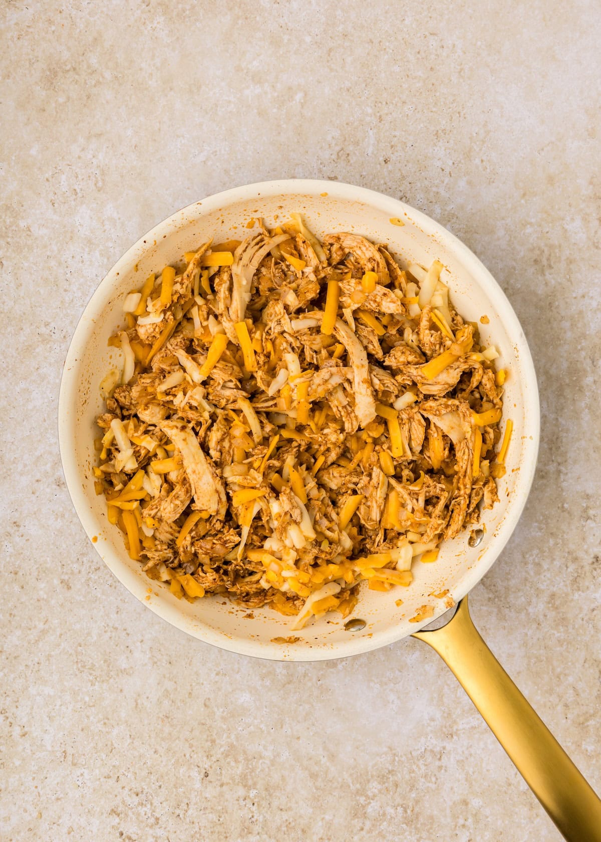 A skillet with shredded chicken, onions, and melted cheese on a light surface.
