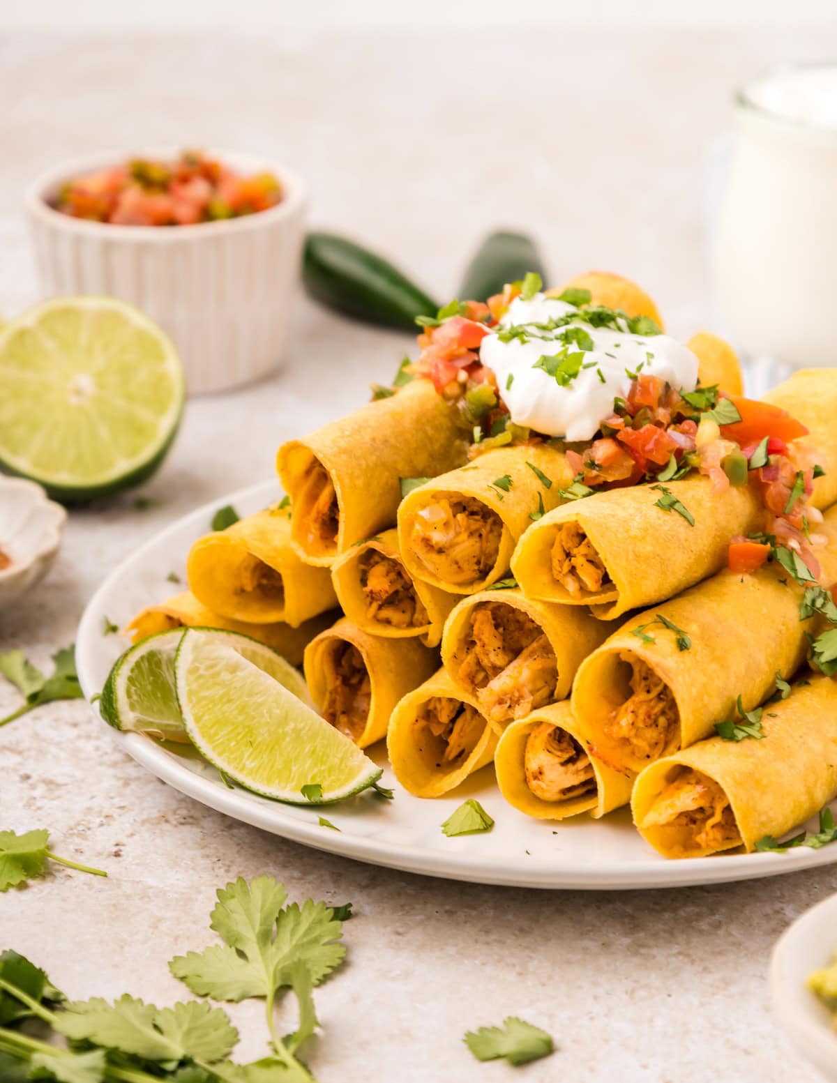 A plate of chicken taquitos topped with sour cream, pico de gallo, and fresh cilantro.