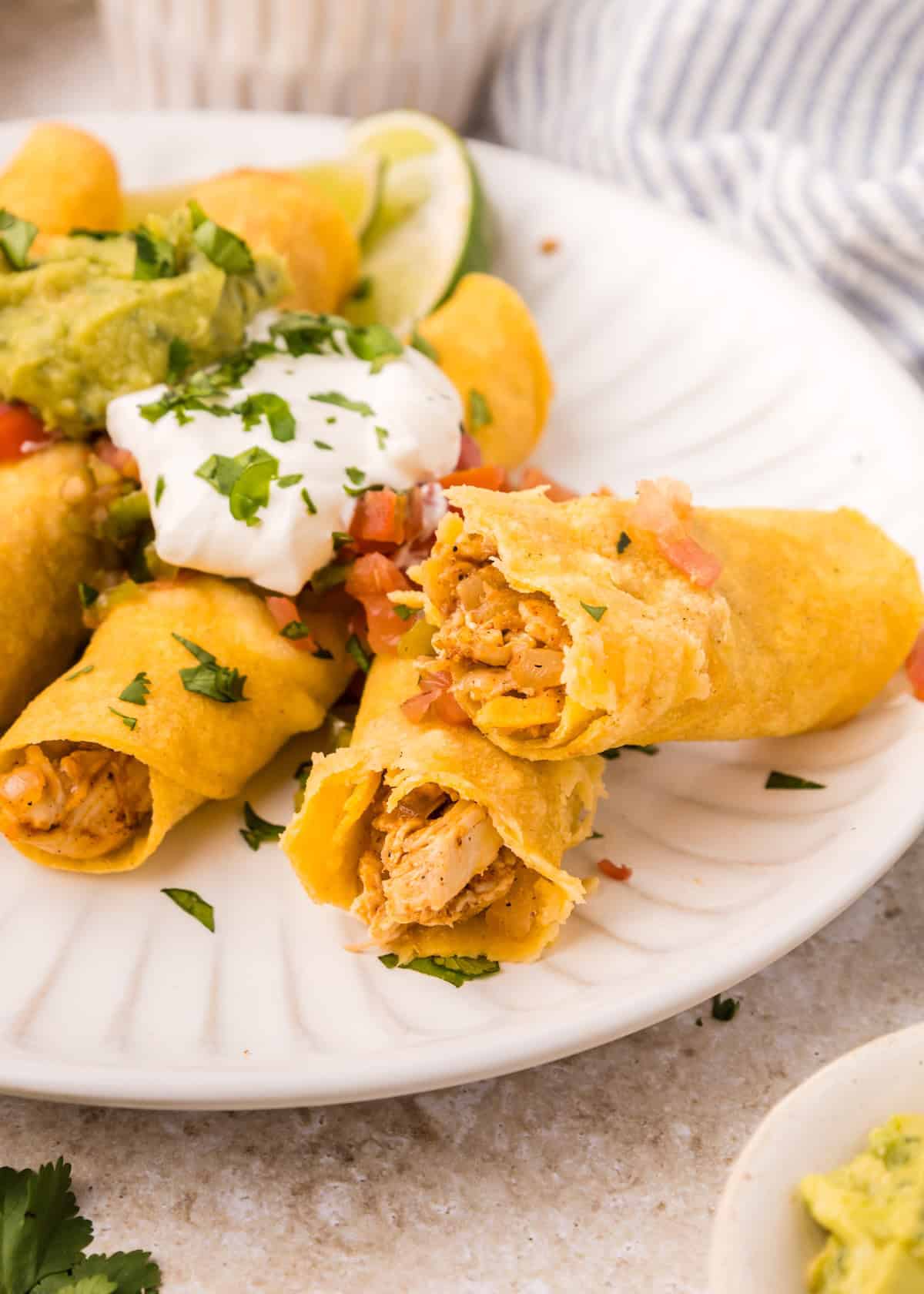 Plate of chicken taquitos topped with sour cream, guacamole, and chopped cilantro.