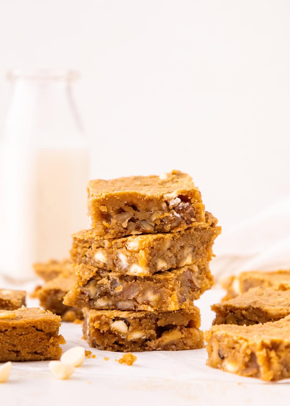 A stack of four blondie bars with nuts, with a bottle of milk in the background.