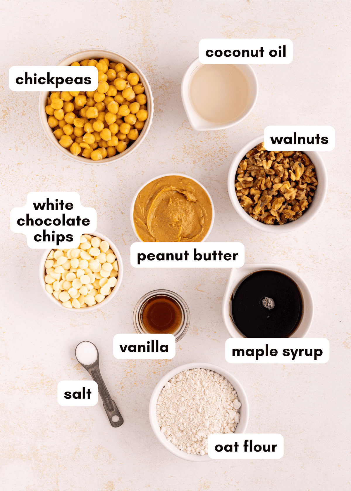 Ingredients for a recipe: chickpeas, coconut oil, walnuts, peanut butter, white chocolate chips, vanilla, maple syrup, salt, oat flour.