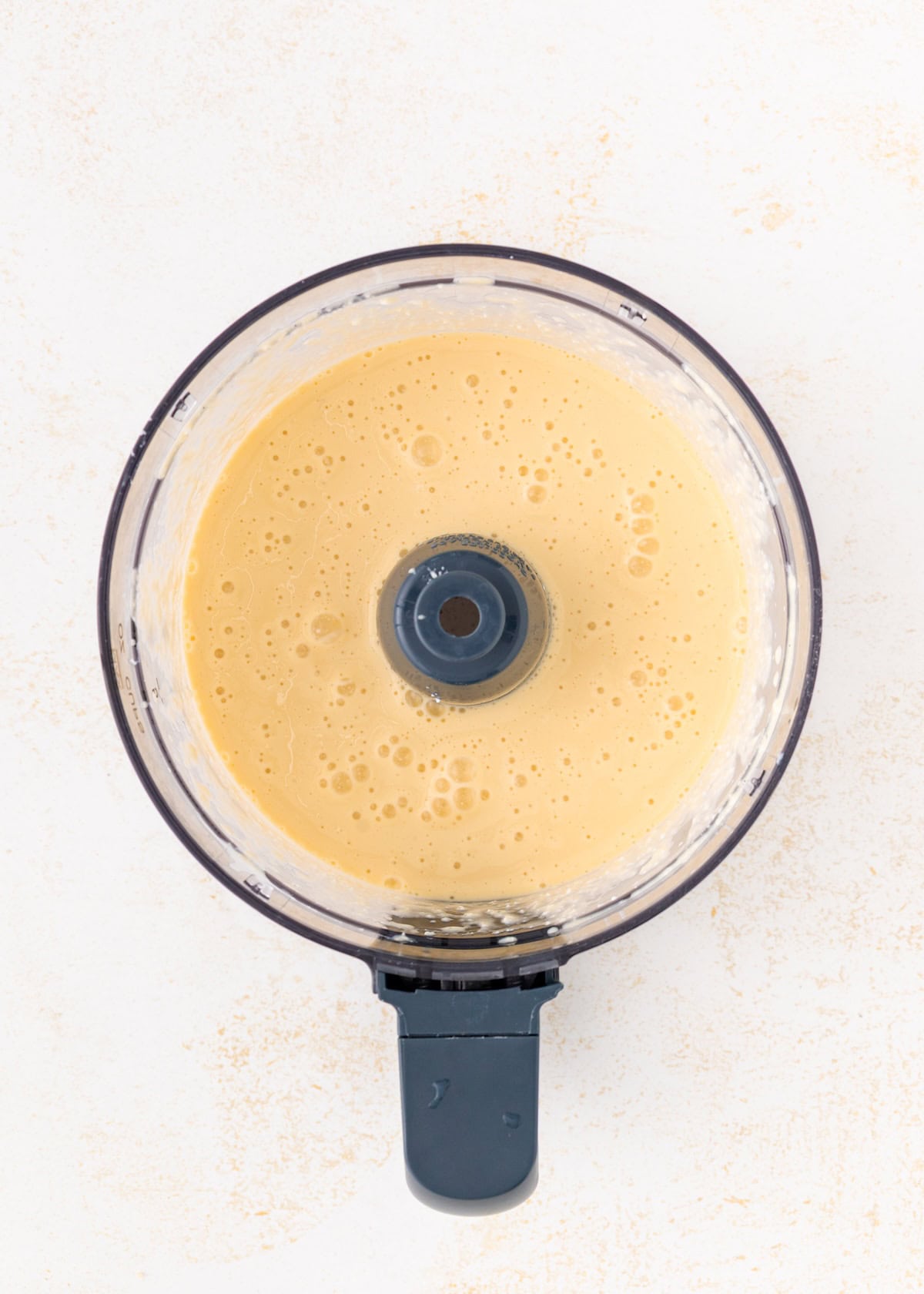 Overhead view of creamy, blended batter in a food processor on a light surface.