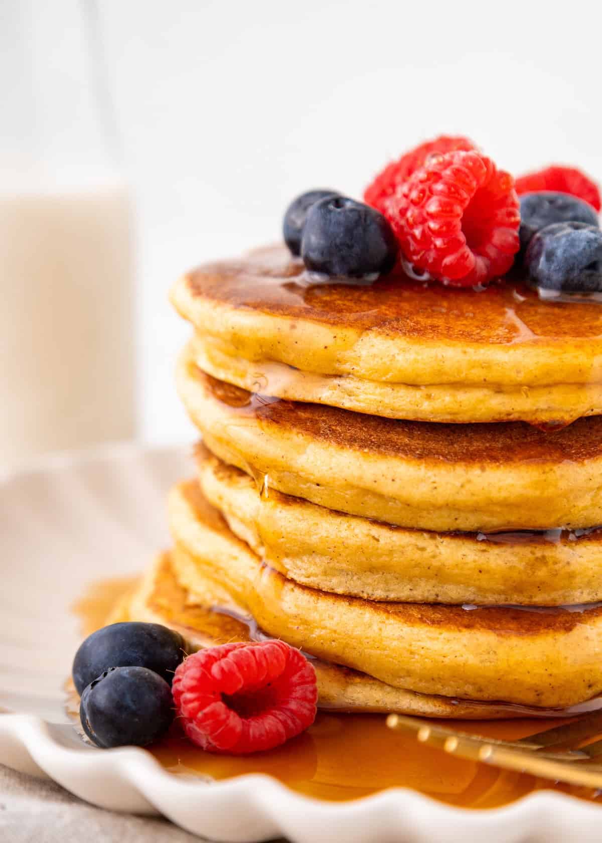 A stack of pancakes topped with blueberries, raspberries, and syrup on a white plate.