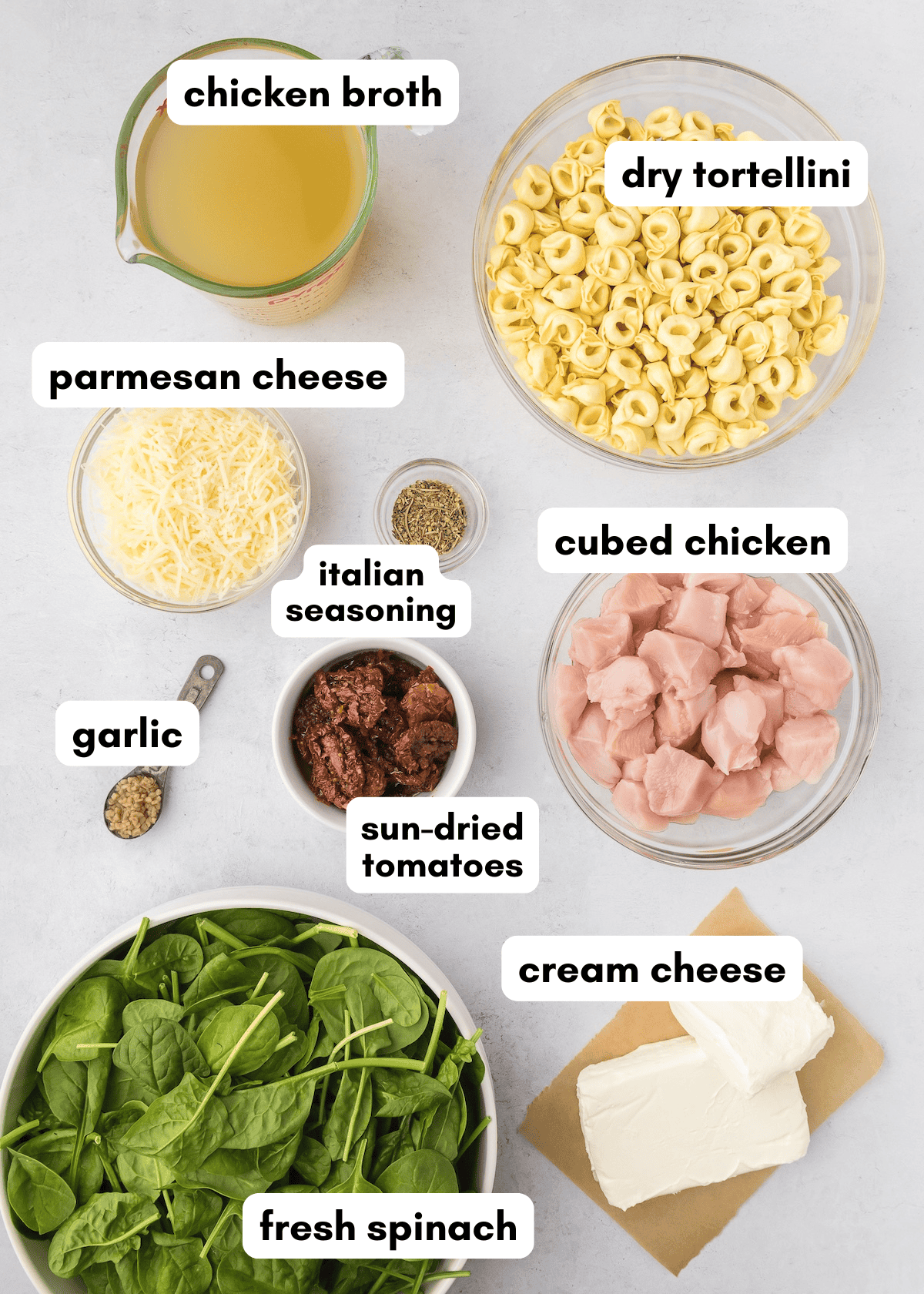 Ingredients for a chicken tortellini dish labeled and arranged on a white surface.