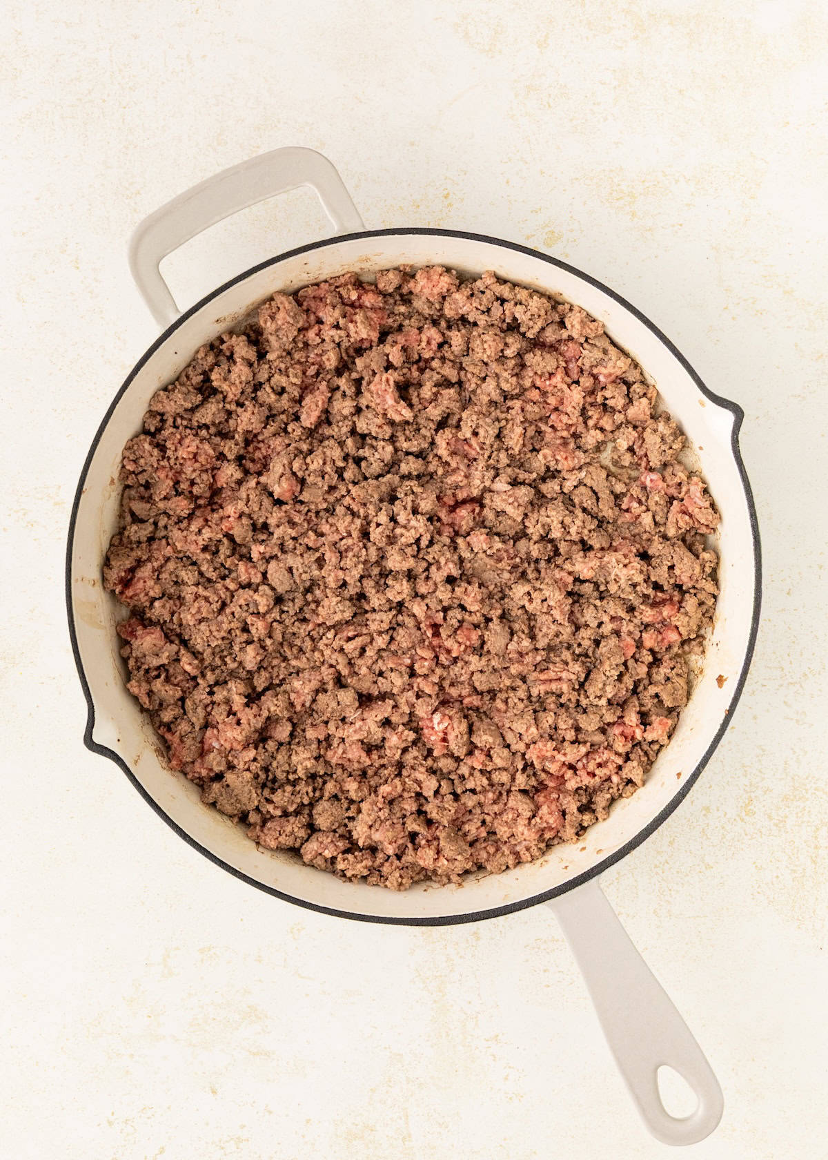 A skillet filled with cooked ground beef on a light-colored surface.