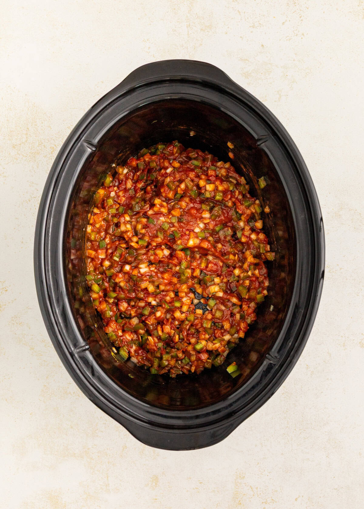Overhead view of chopped vegetables and tomato sauce in a black slow cooker.