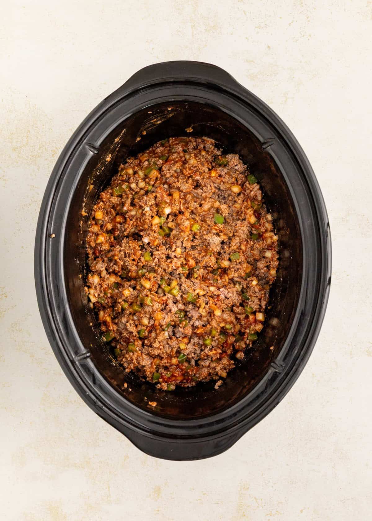 Ground beef, vegetables, and sauce mixture cooking in a black slow cooker, top view.
