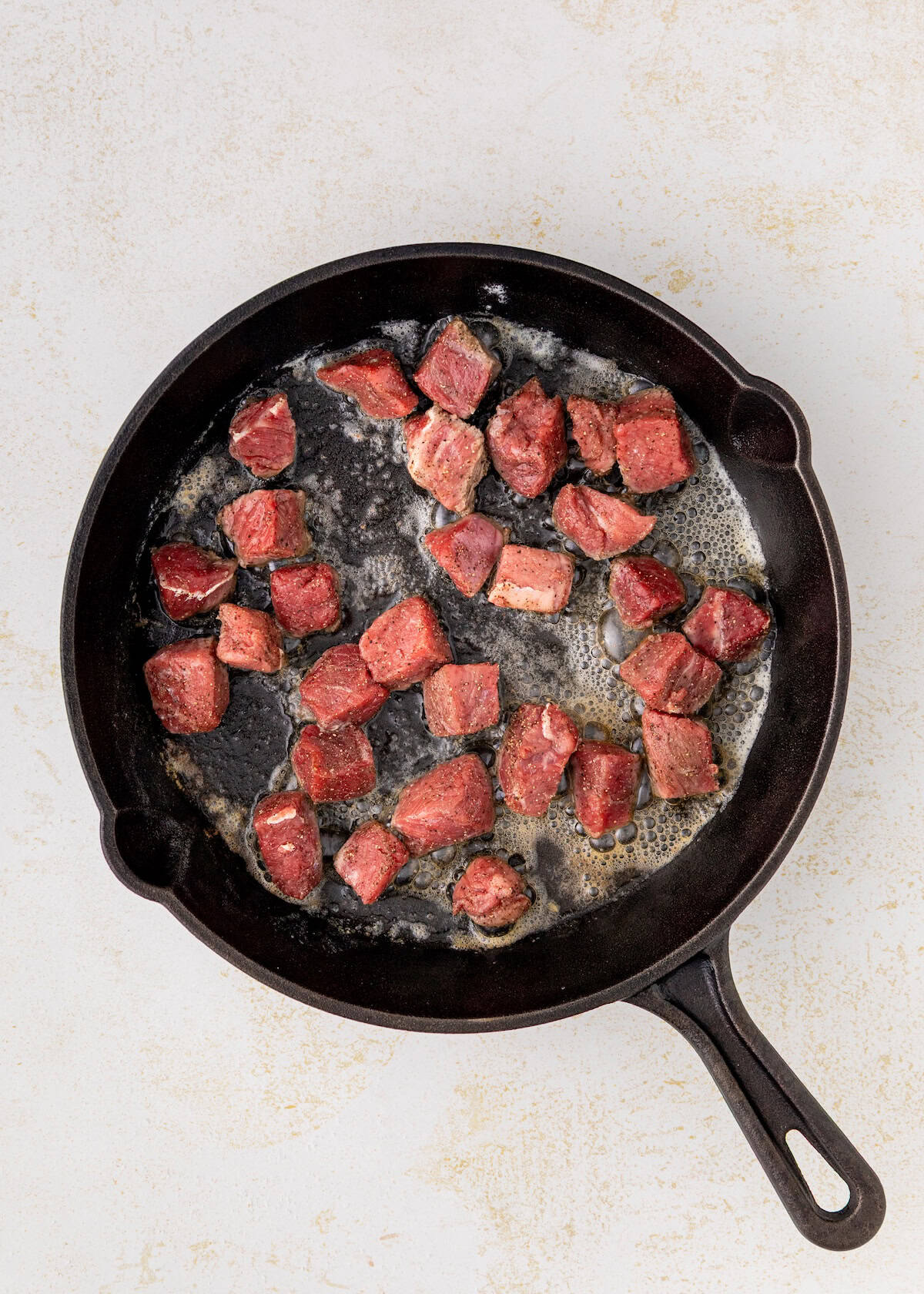 Cubed meat sizzling in a black cast iron skillet with bubbling butter.