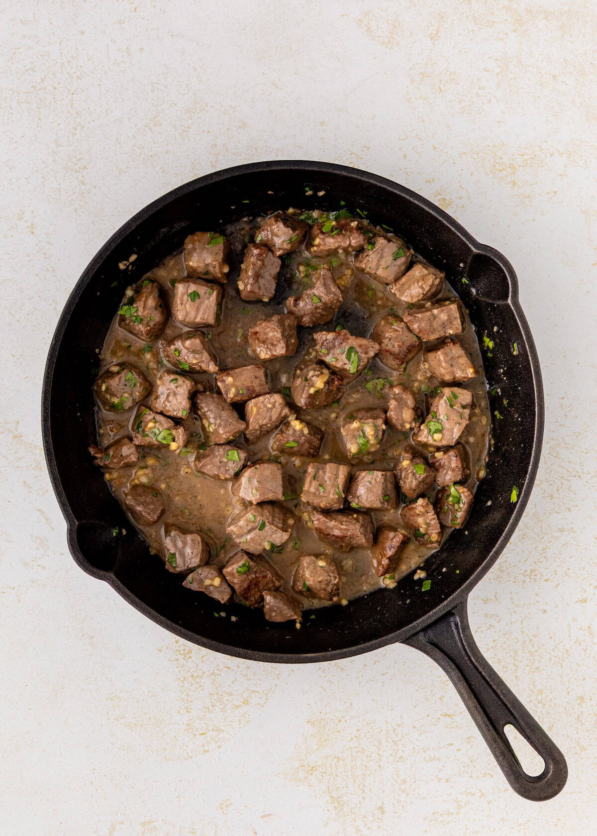 Cubed steak pieces in sauce cooking in a black cast iron skillet on a light surface.