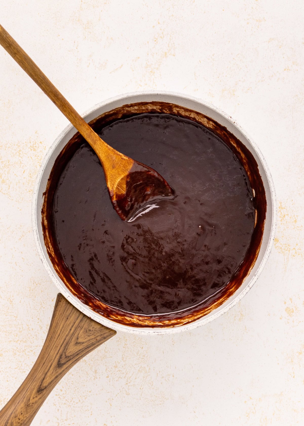 A saucepan of German chocolate brownies sauce with a wooden spoon on a white background.