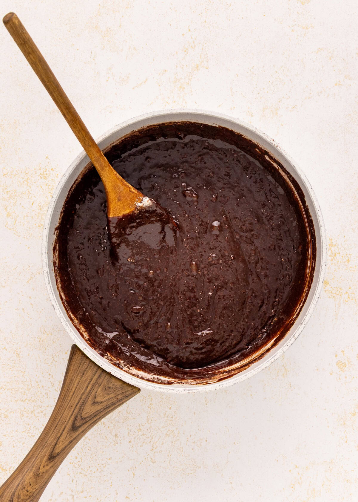 A saucepan of German chocolate brownies batter with a wooden spoon on a light background.
