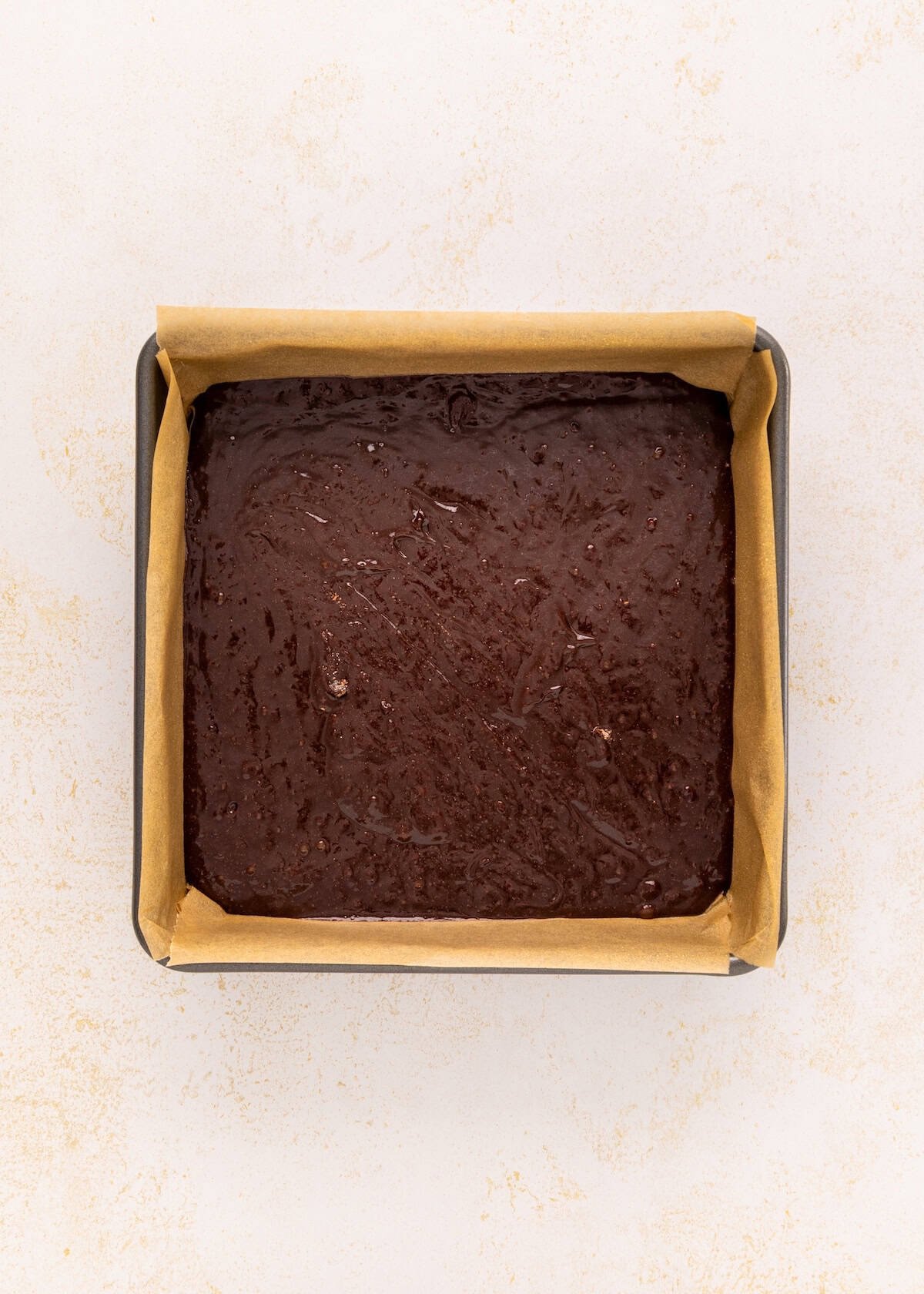 German chocolate brownies batter in a parchment-lined pan on a light surface.
