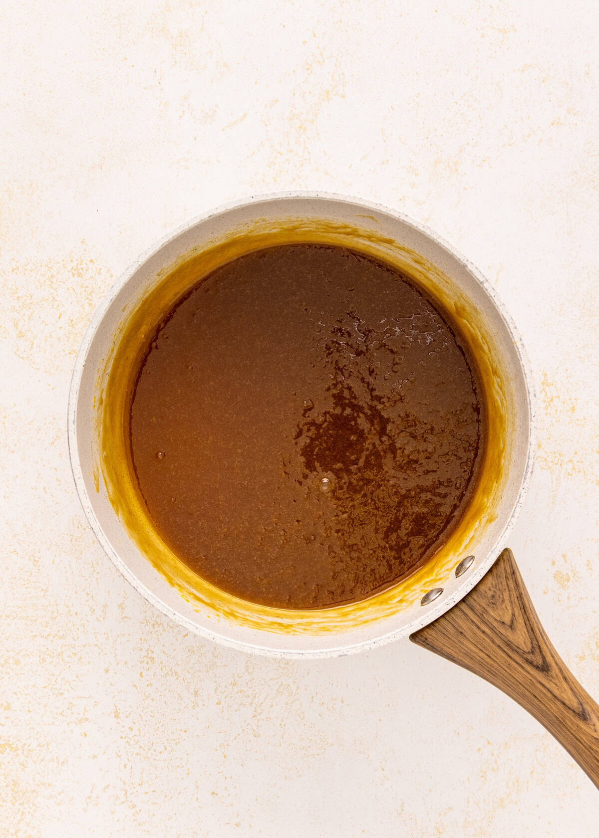 A saucepan with brown caramel sauce for German chocolate brownies on a light-colored surface.