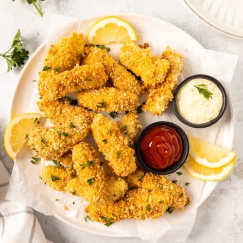 Plate of crispy Homemade Fish Sticks with lemon slices, ketchup, and mayonnaise for dipping.