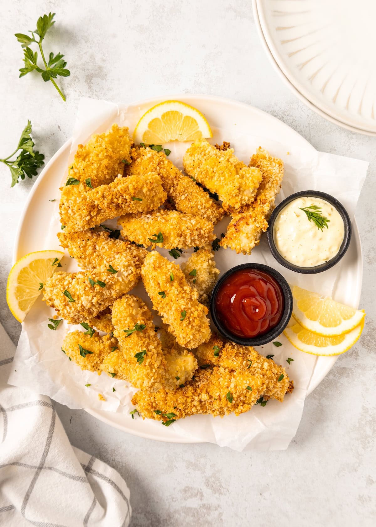 Plate of crispy Homemade Fish Sticks with lemon slices, ketchup, and mayonnaise for dipping.