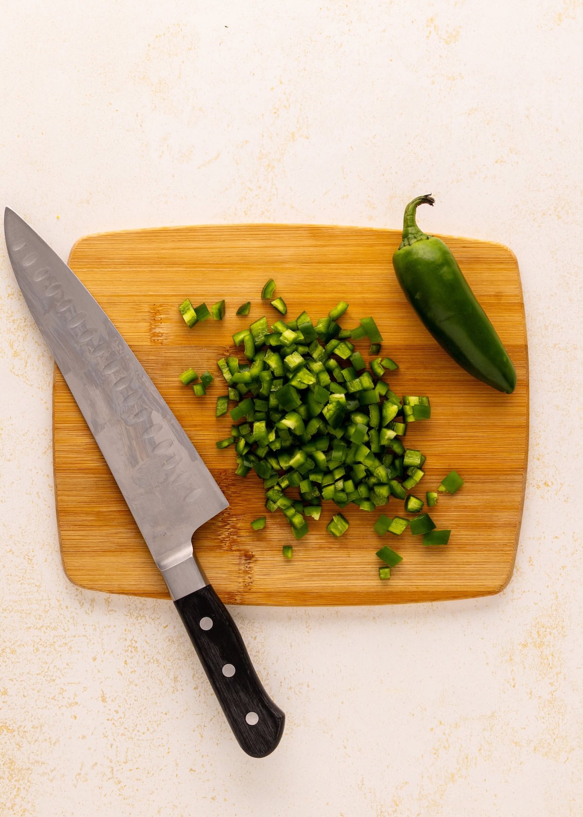 A jalapeño, diced pieces, and a knife on a wooden cutting board.