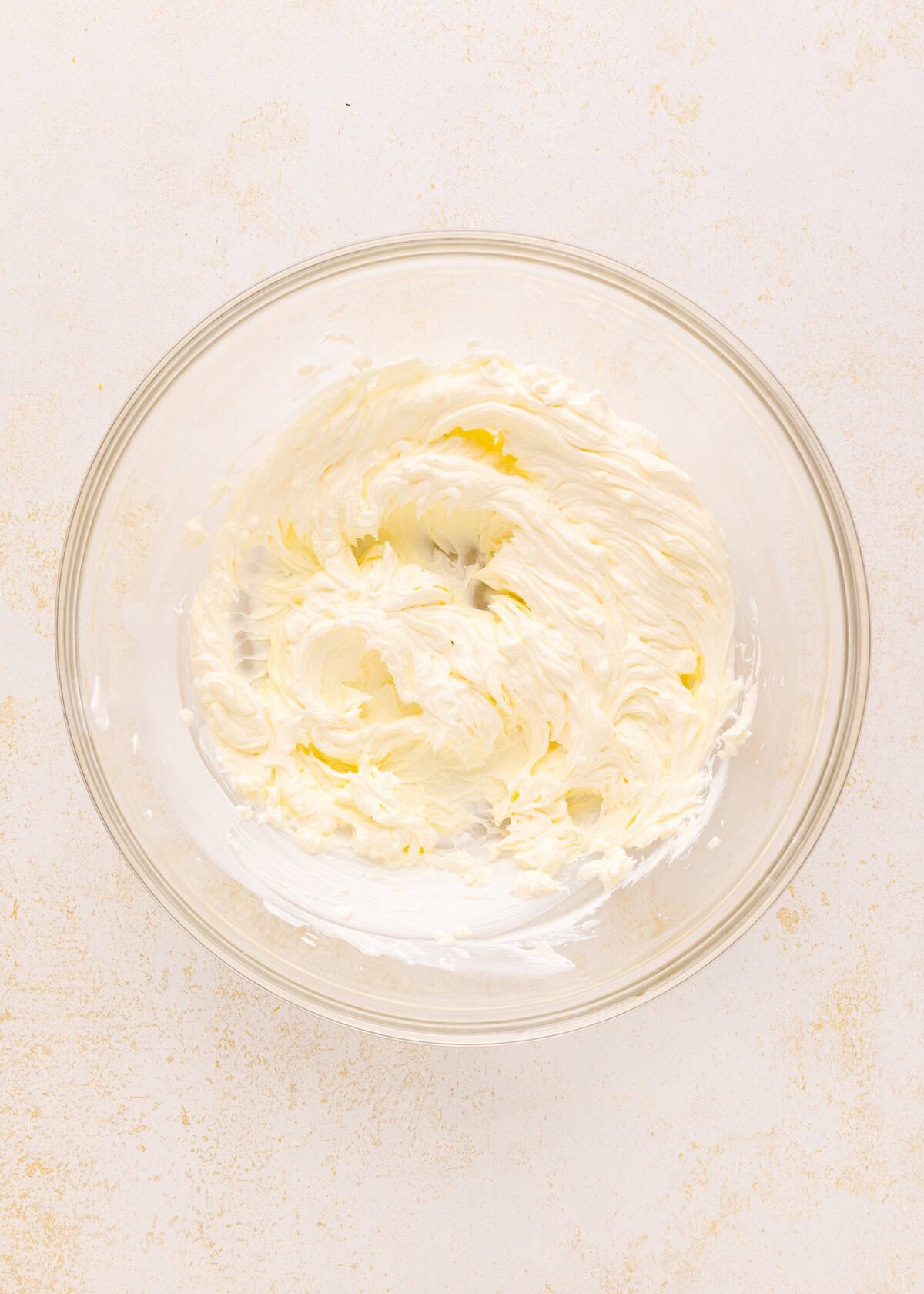A glass bowl with whipped cream cheese on a light textured surface.