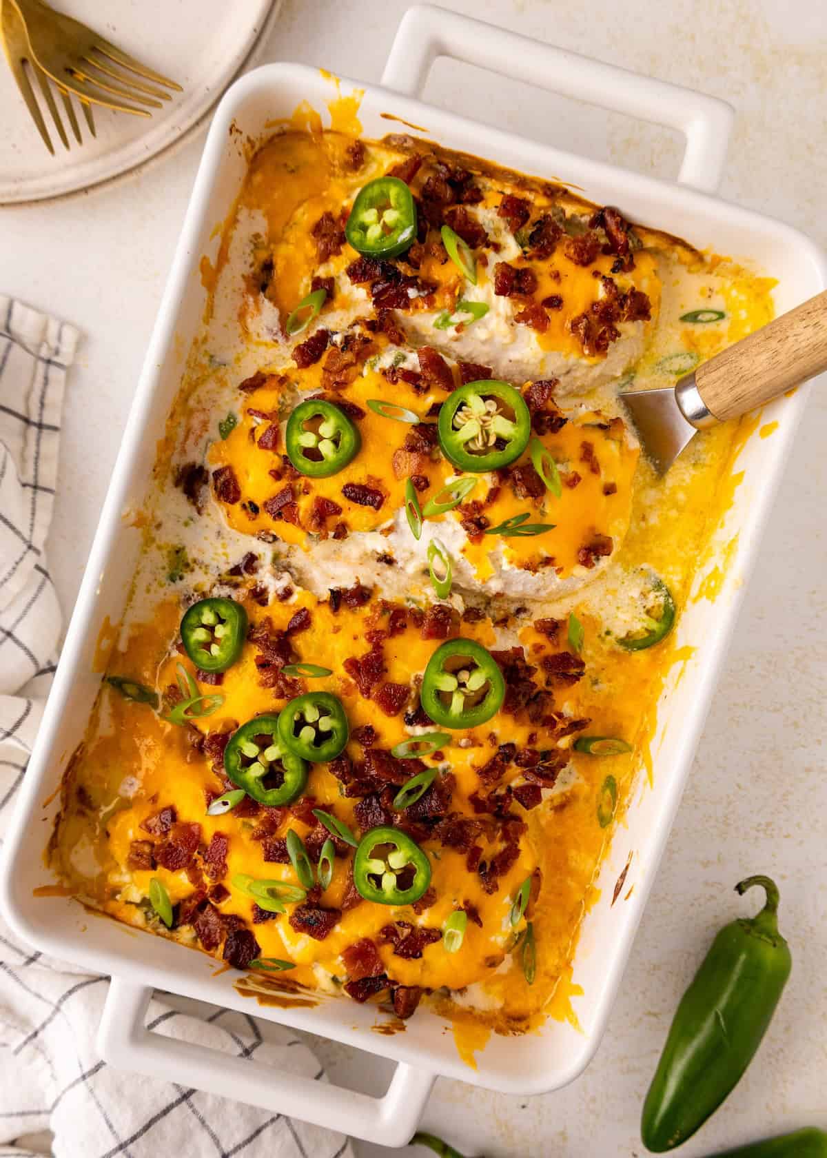 Casserole topped with melted cheese, bacon, jalapeño slices, and green onions in a white dish.