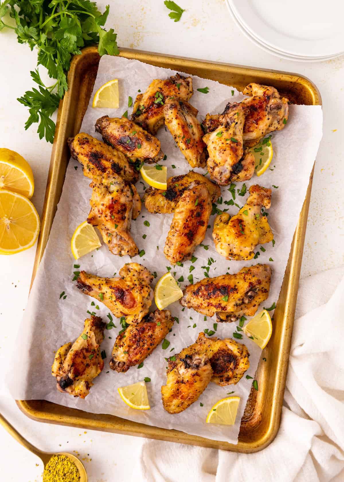 Baked chicken wings on a tray with lemon wedges and chopped herbs, overhead view.