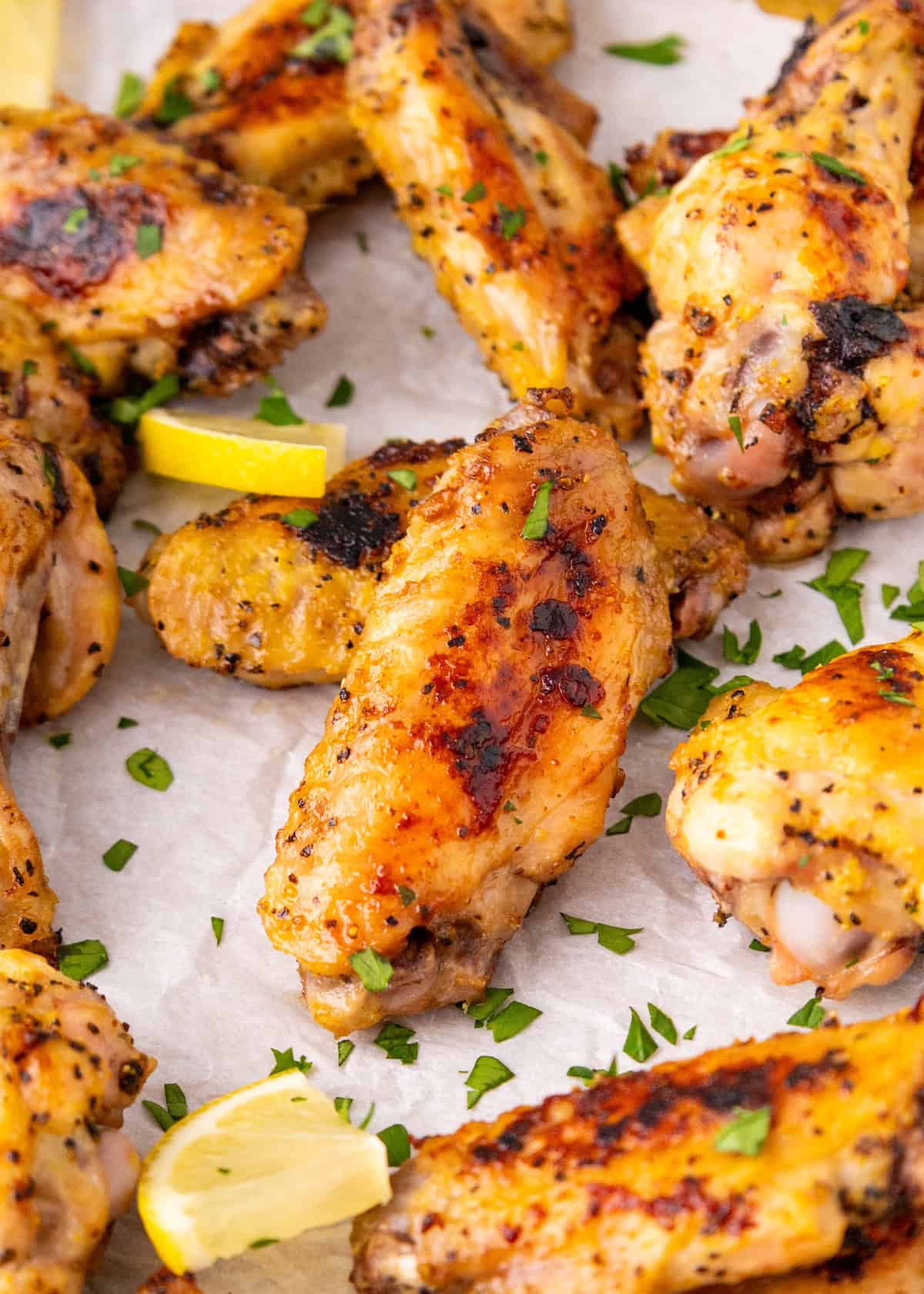 Golden baked chicken wings with herbs and lemon wedges on parchment paper.