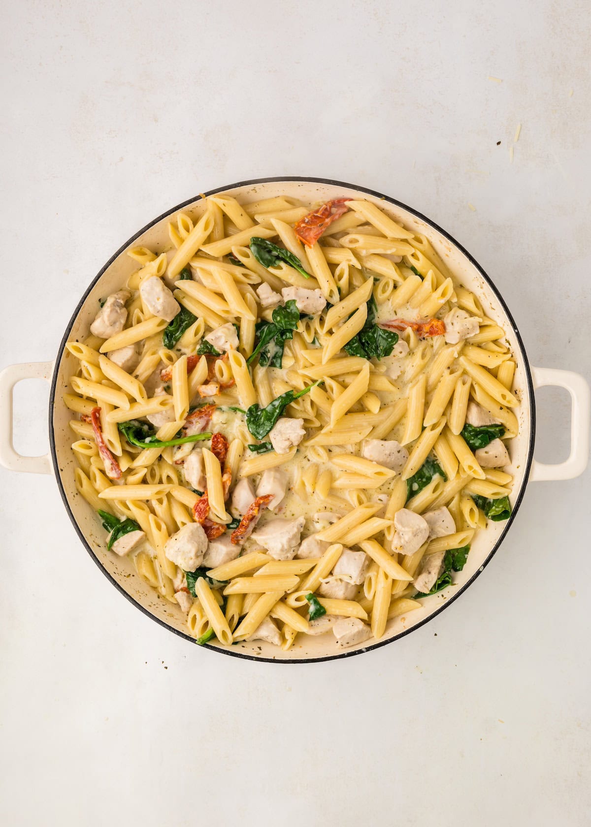 Large pot of creamy penne pasta with chicken, spinach, and sun-dried tomatoes.