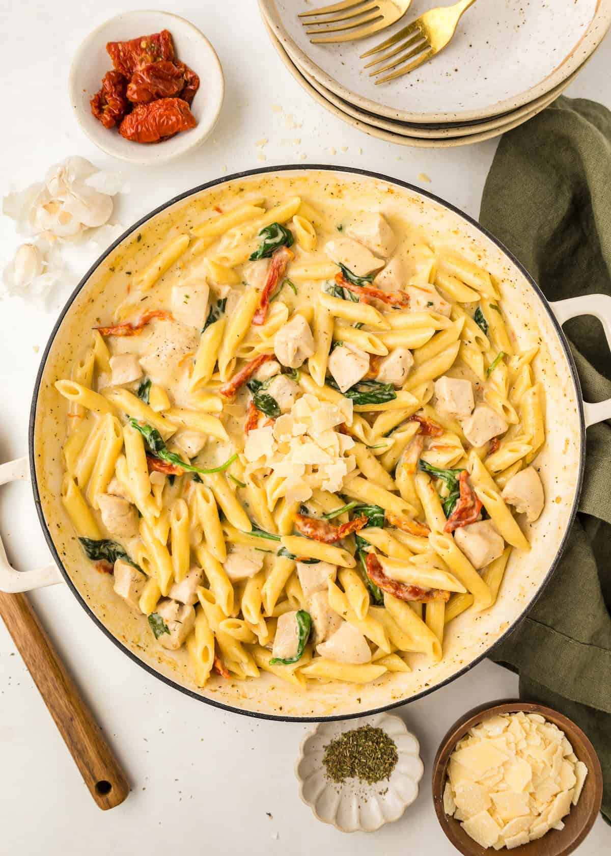 Creamy penne pasta with chicken, spinach, and sun-dried tomatoes in a white skillet.