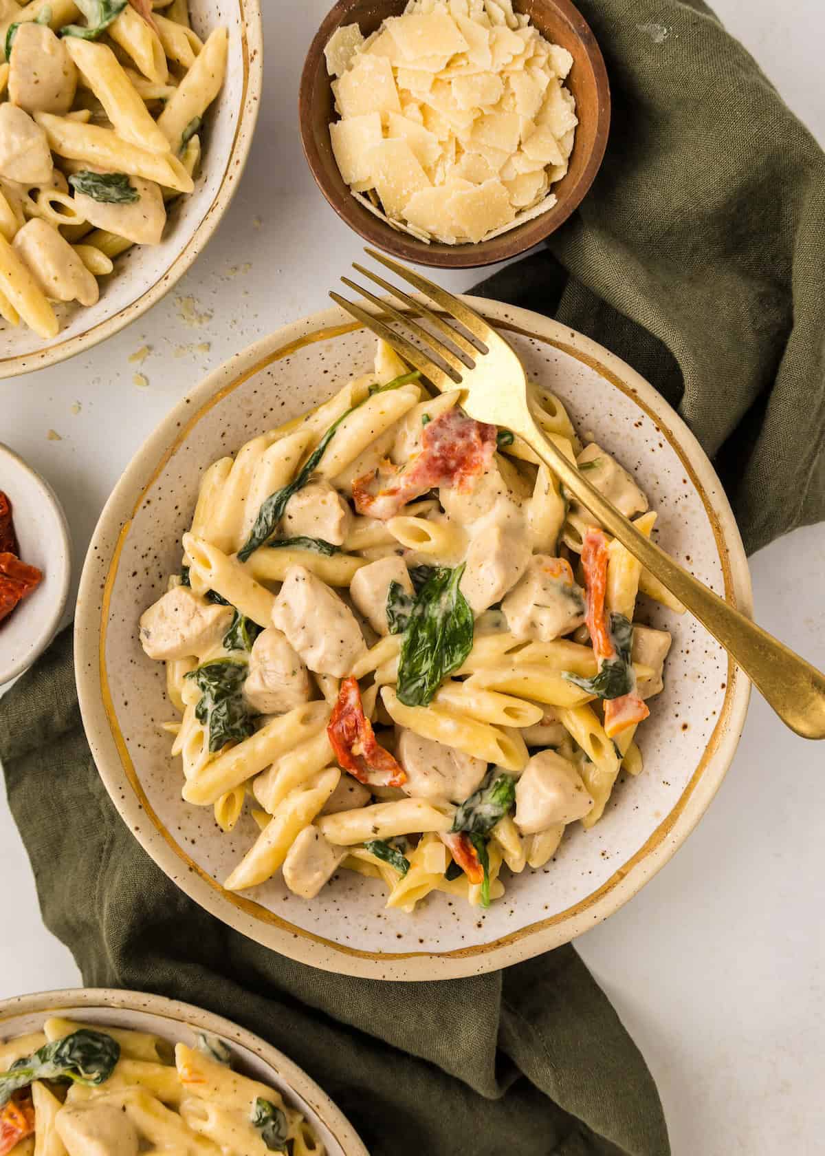 Plate of creamy penne pasta with chicken, spinach, sun-dried tomatoes, and a bowl of parmesan.