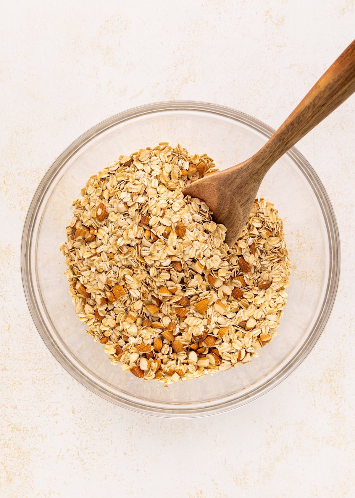 A glass bowl of Vanilla Almond Granola with a wooden spoon on a light surface.
