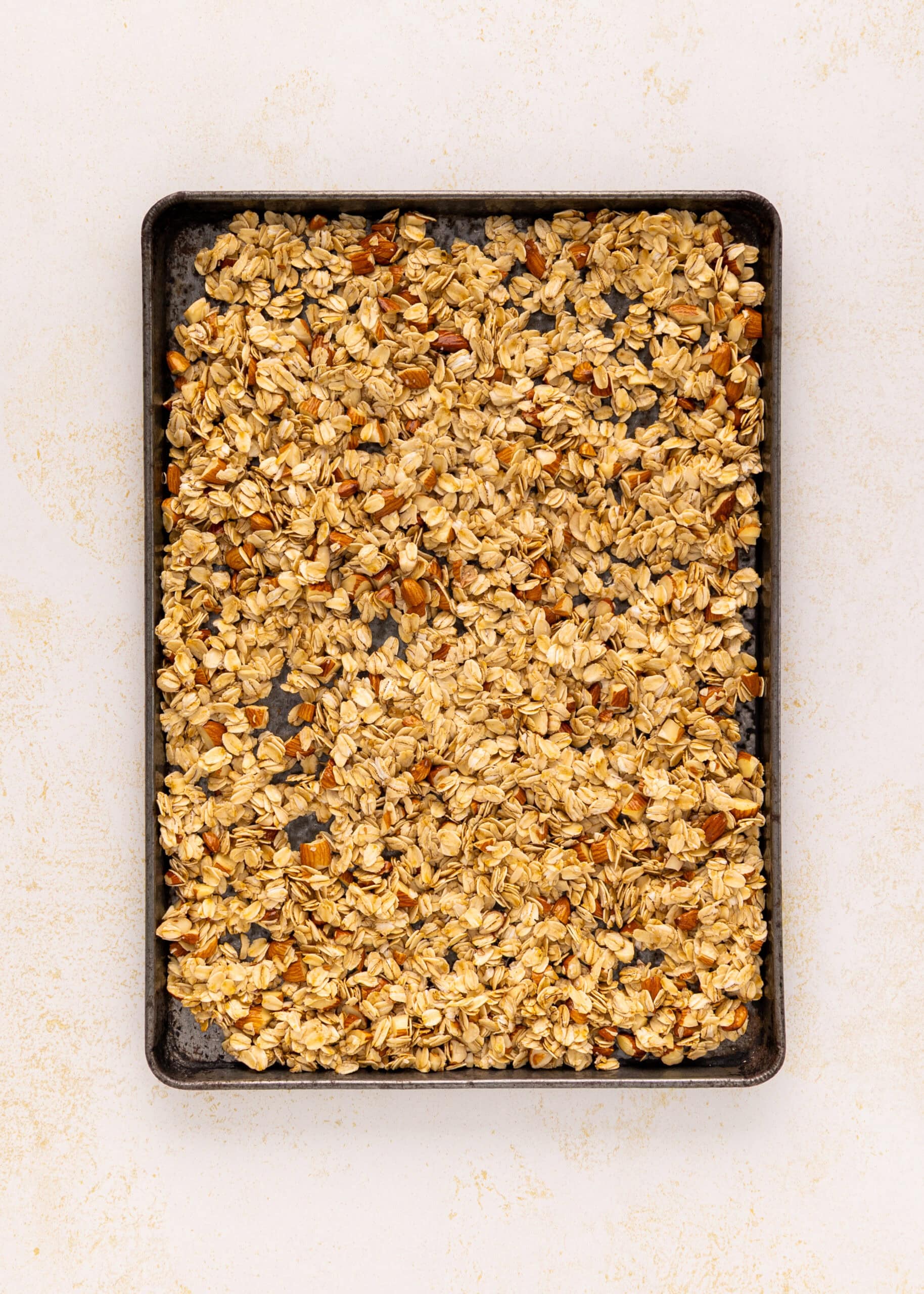 A baking tray filled with uncooked Vanilla Almond Granola on a light surface.