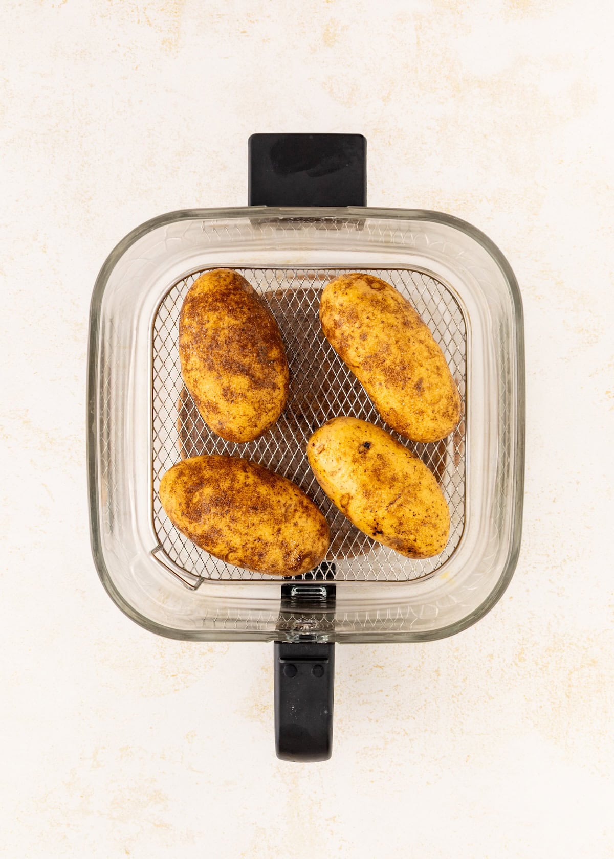 Four seasoned potatoes in an air fryer basket, viewed from above on a light background.