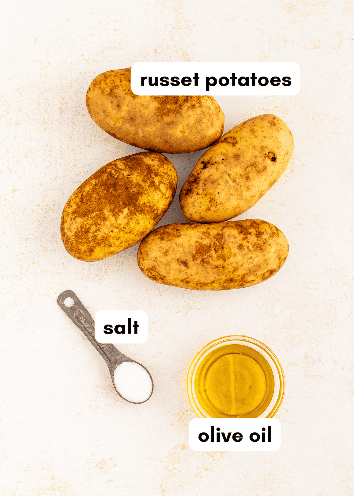 Air Fryer Baked Potatoes: Four russet potatoes, olive oil, and salt on a white surface.