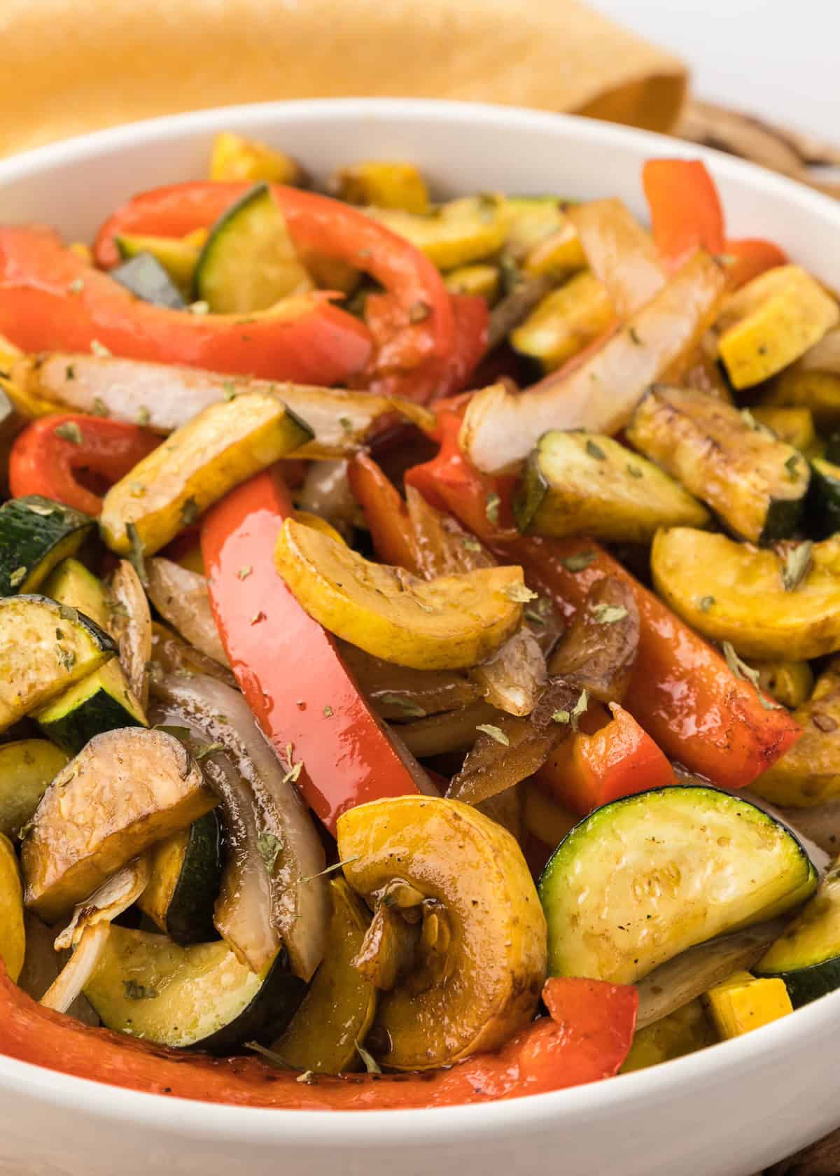 Colorful roasted vegetables including zucchini, red bell pepper, onion, and yellow squash in a bowl.